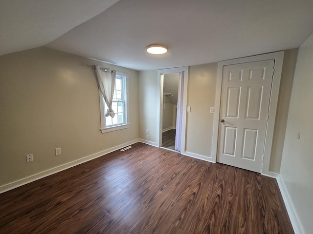 unfurnished bedroom featuring a walk in closet, vaulted ceiling, baseboards, a closet, and dark wood-type flooring