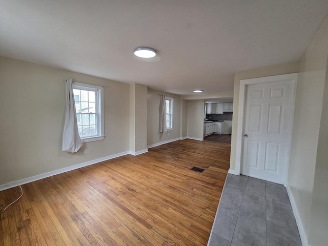 unfurnished living room featuring baseboards, dark wood-style floors, and plenty of natural light