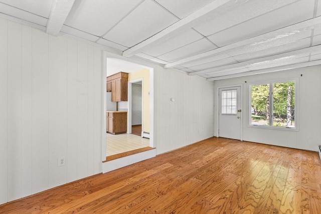 unfurnished room featuring light wood-style floors, baseboard heating, and wood walls