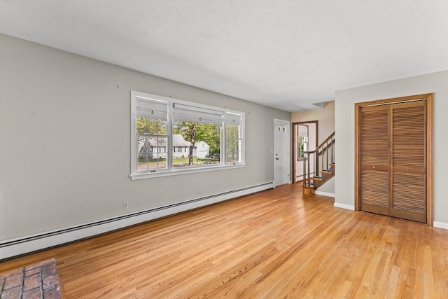 unfurnished living room featuring a baseboard heating unit, wood finished floors, stairs, and baseboards