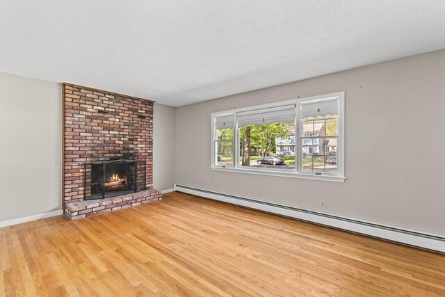 unfurnished living room with wood finished floors, a baseboard heating unit, a brick fireplace, and baseboards