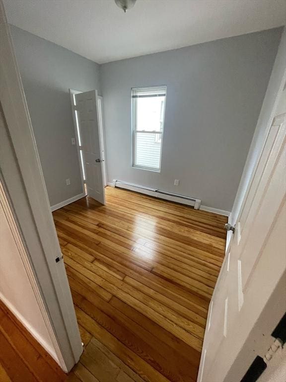 unfurnished bedroom featuring baseboards, a baseboard heating unit, and hardwood / wood-style floors