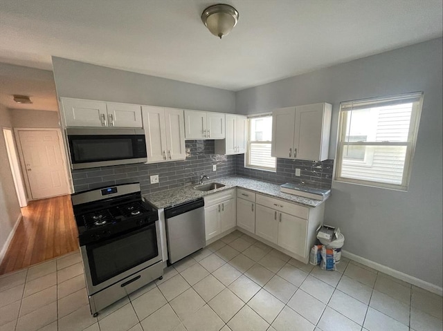 kitchen featuring appliances with stainless steel finishes, a sink, white cabinetry, baseboards, and backsplash