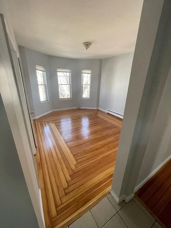 empty room featuring baseboards, light wood-style flooring, and a baseboard radiator