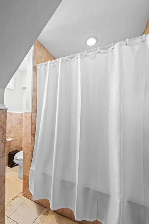 bathroom with tile patterned floors, a shower with curtain, toilet, and tile walls