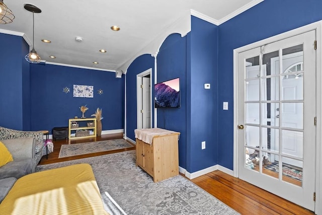 living area with arched walkways, crown molding, baseboards, and wood finished floors