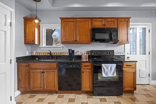 kitchen featuring dark stone counters, a sink, black appliances, pendant lighting, and brown cabinets