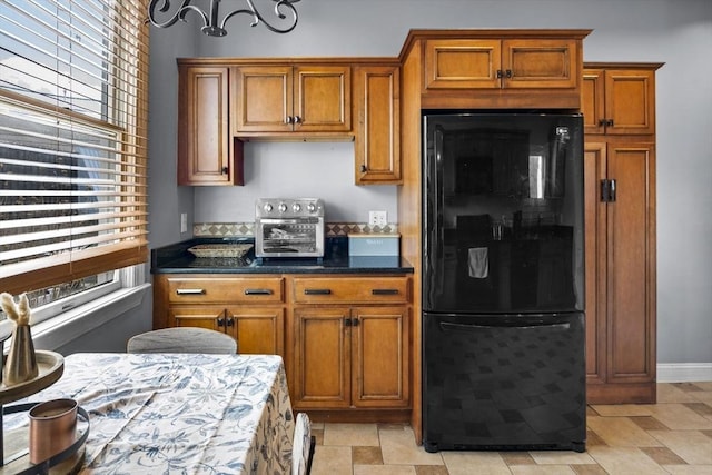 kitchen featuring brown cabinets, dark stone countertops, stone finish flooring, freestanding refrigerator, and a toaster