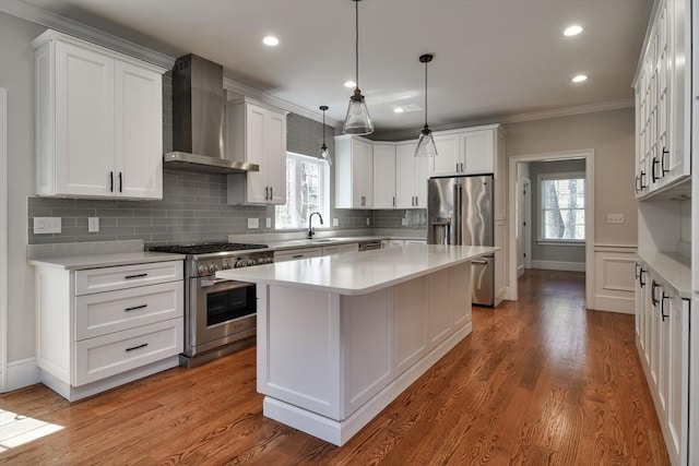 kitchen with wall chimney range hood, high quality appliances, a sink, light countertops, and ornamental molding