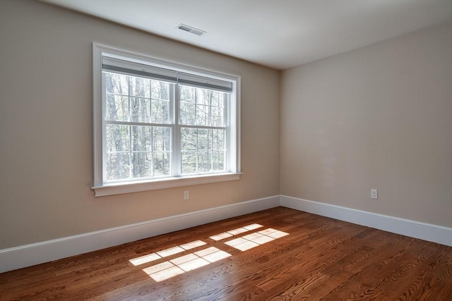 unfurnished room with baseboards, visible vents, plenty of natural light, and wood finished floors