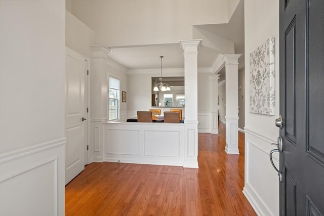 foyer with a decorative wall, light wood-style flooring, a wainscoted wall, and decorative columns