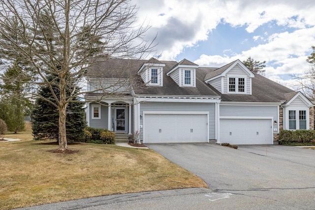 cape cod-style house with a front yard, an attached garage, driveway, and roof with shingles