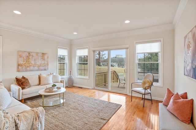 living area with baseboards, a healthy amount of sunlight, crown molding, and hardwood / wood-style flooring