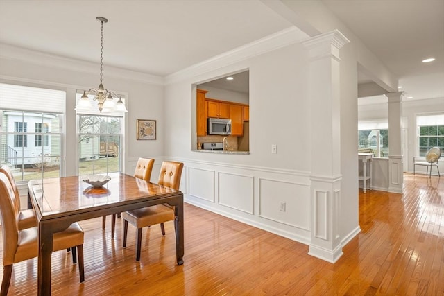 dining space featuring ornate columns, an inviting chandelier, light wood-style floors, crown molding, and a decorative wall