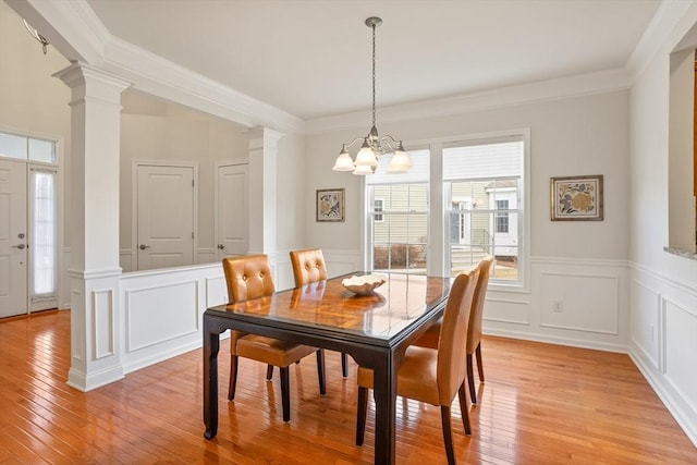 dining room with a notable chandelier, light wood-style flooring, ornate columns, and ornamental molding