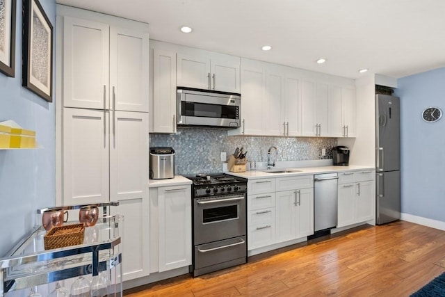 kitchen with decorative backsplash, appliances with stainless steel finishes, a sink, light countertops, and white cabinets