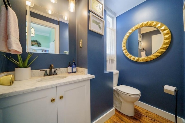 bathroom featuring baseboards, wood finished floors, toilet, vanity, and ornamental molding