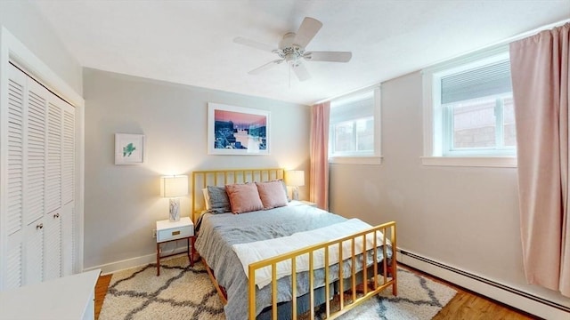 bedroom featuring a baseboard radiator, a closet, baseboards, wood finished floors, and a ceiling fan