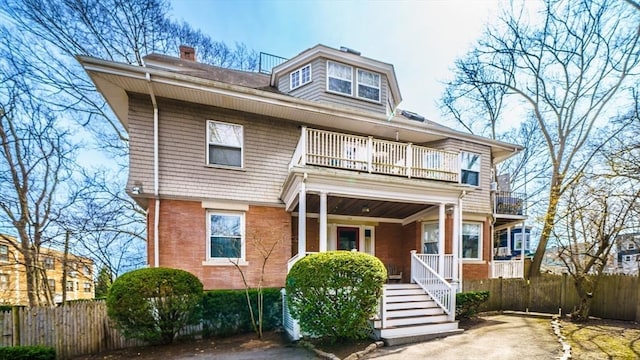 back of property featuring a balcony, fence, covered porch, and a chimney
