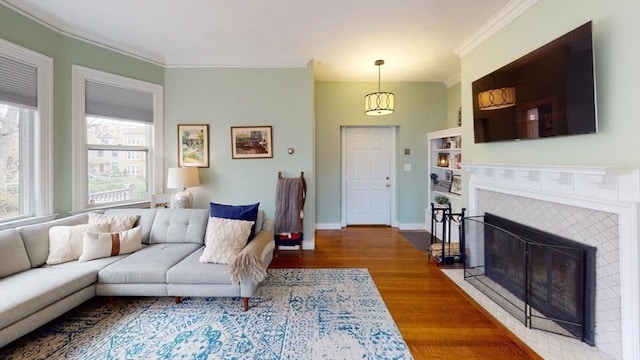 living area with wood finished floors, ornamental molding, a tiled fireplace, and baseboards