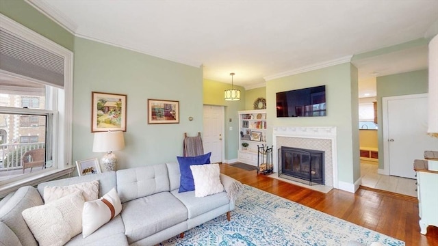 living room featuring ornamental molding, wood finished floors, a tiled fireplace, and baseboards