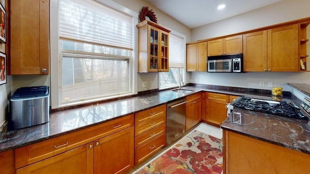 kitchen featuring stainless steel appliances, a sink, open shelves, dark stone countertops, and brown cabinets