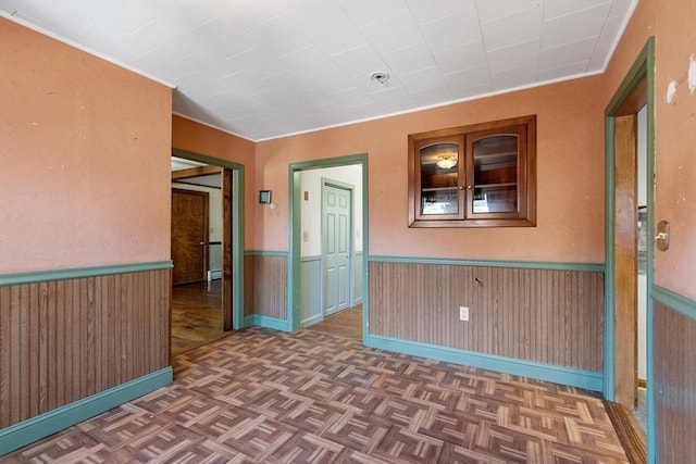 spare room with parquet floors, wooden walls, and wainscoting