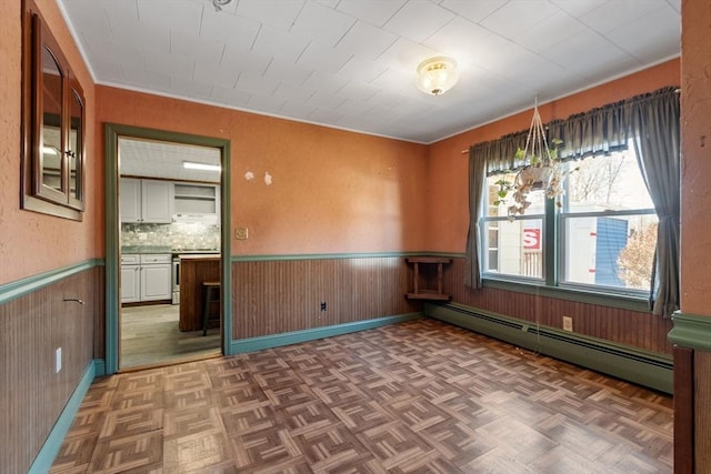 empty room with a baseboard heating unit, wooden walls, a wainscoted wall, and parquet flooring