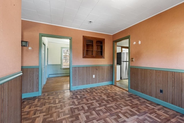 empty room featuring a wainscoted wall, wood walls, and a baseboard heating unit