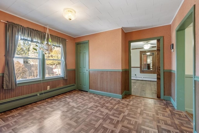 empty room with a baseboard heating unit, baseboard heating, a wainscoted wall, and wooden walls