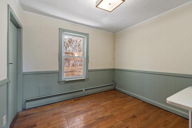 spare room featuring a baseboard heating unit, ornamental molding, wood-type flooring, and wainscoting