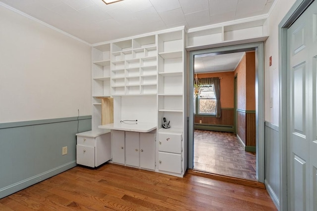 unfurnished office featuring crown molding, light wood-type flooring, a baseboard radiator, and wainscoting