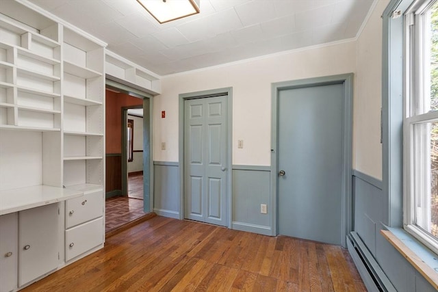 interior space featuring a wainscoted wall, ornamental molding, a baseboard heating unit, and wood-type flooring