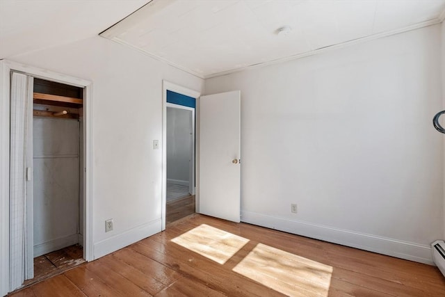 unfurnished bedroom featuring baseboard heating, baseboards, and wood-type flooring