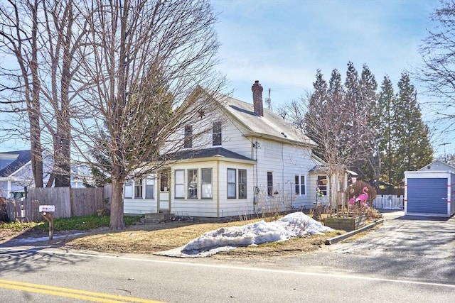 view of front facade with a storage unit, entry steps, fence, an outdoor structure, and a chimney