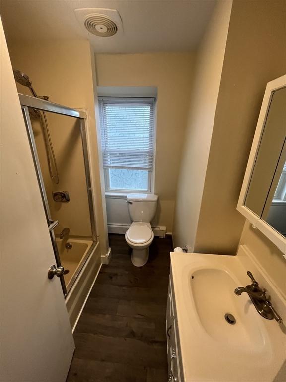 full bathroom with combined bath / shower with glass door, wood-type flooring, vanity, and toilet