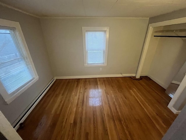 unfurnished bedroom featuring wood-type flooring, crown molding, multiple windows, and a baseboard heating unit