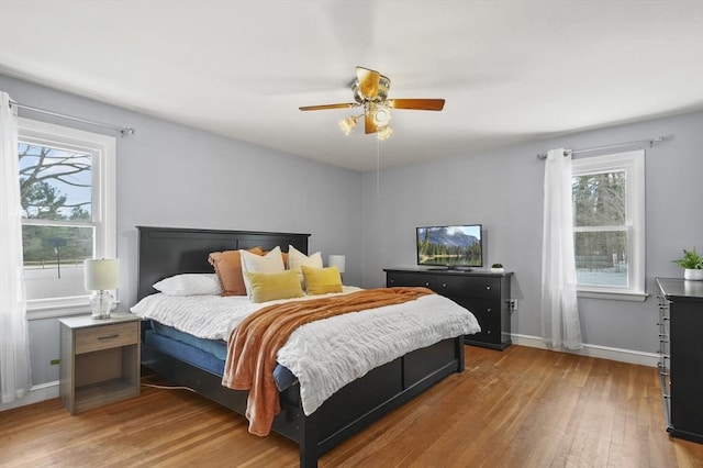 bedroom with ceiling fan, multiple windows, baseboards, and wood finished floors