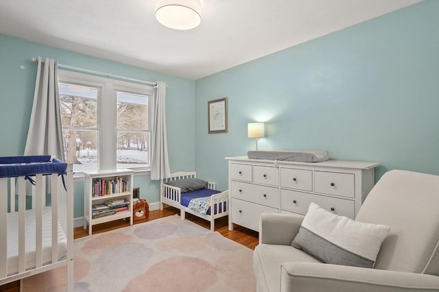 bedroom featuring a nursery area, baseboards, and wood finished floors