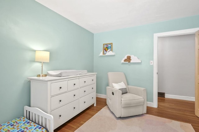 bedroom featuring a crib, visible vents, baseboards, and wood finished floors