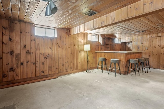 bar featuring a bar, concrete floors, wood ceiling, and wooden walls