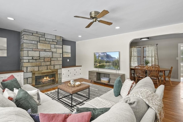 living room with baseboards, arched walkways, wood finished floors, a stone fireplace, and recessed lighting