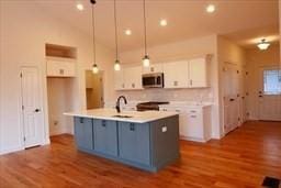 kitchen featuring stainless steel microwave, white cabinets, a sink, and wood finished floors