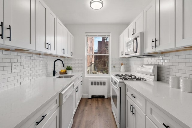 kitchen featuring radiator, white appliances, sink, white cabinetry, and light wood-type flooring