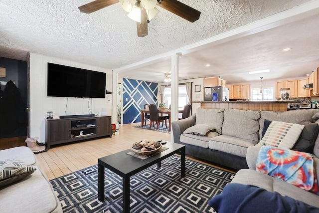 living room featuring ceiling fan, light hardwood / wood-style floors, decorative columns, and a textured ceiling