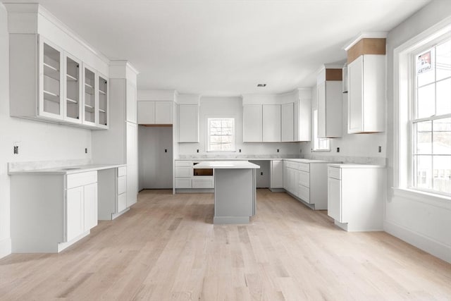 kitchen with a center island, baseboards, white cabinets, light wood finished floors, and glass insert cabinets