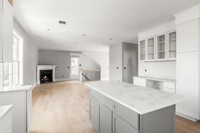 kitchen featuring light wood-type flooring, gray cabinetry, light countertops, glass insert cabinets, and white cabinetry