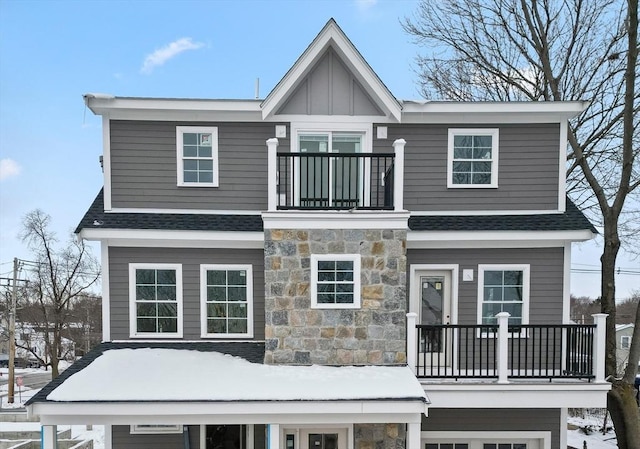 view of front of house with board and batten siding, roof with shingles, a balcony, and stone siding