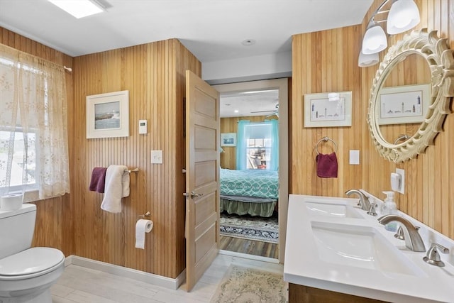 bathroom featuring toilet, wood walls, and vanity