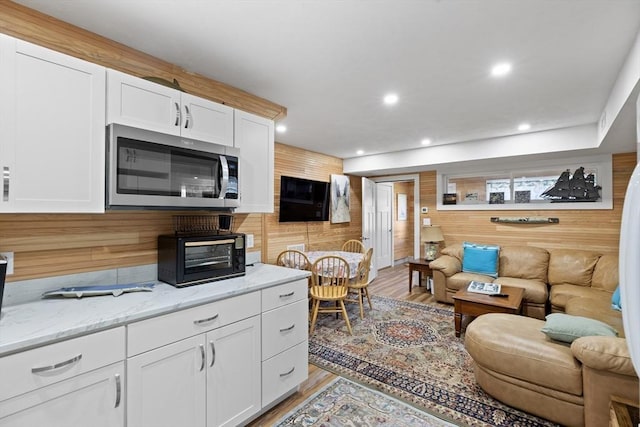 kitchen featuring light stone countertops, white cabinets, wood walls, and light wood-type flooring